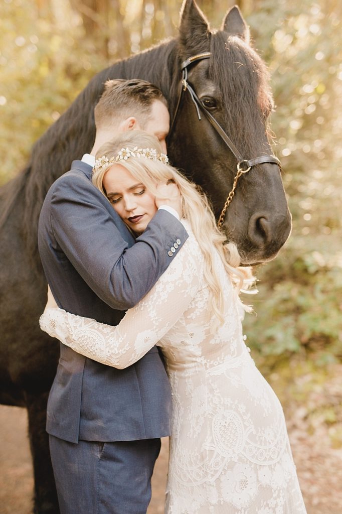 Bride and groom embracing next to a black Friesian horse