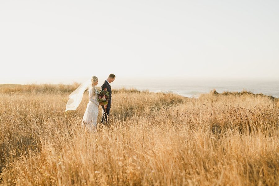 Bride and groom walking in a field overlooking the ocean in Mendocino California