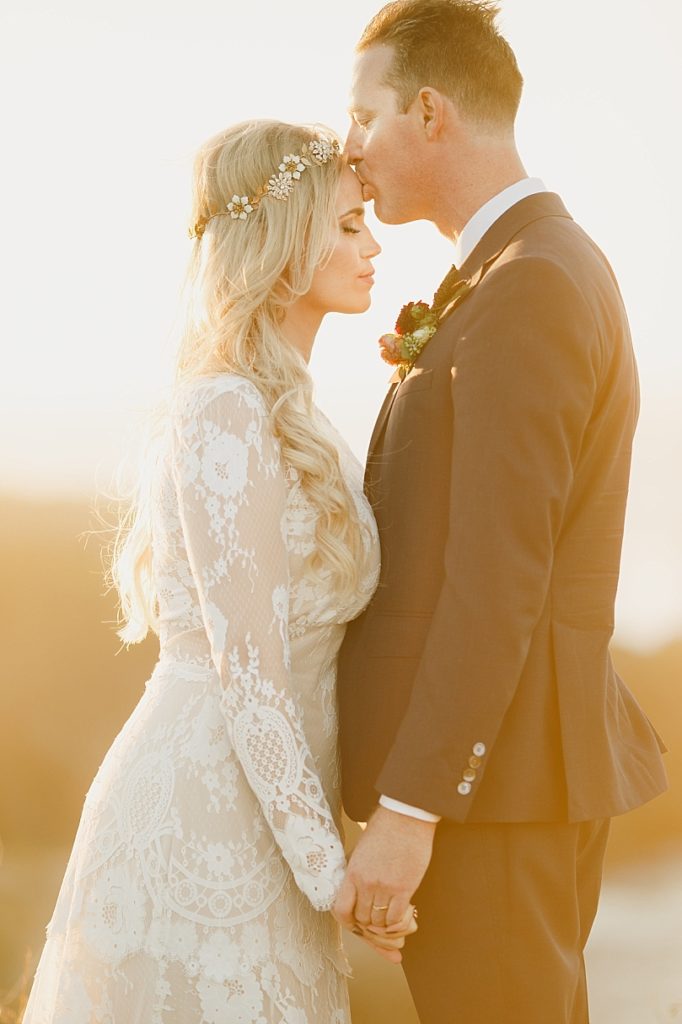 Romantic photo of groom kissing brides forehead in golden sunset light