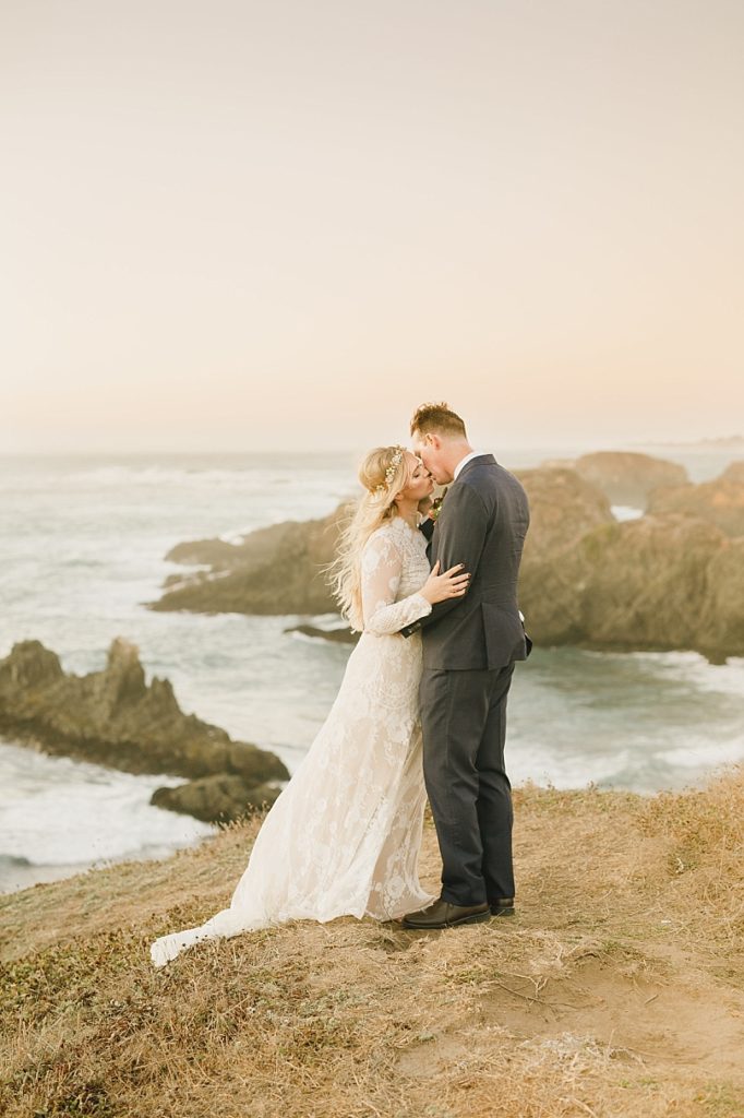 Romantic photo of bride and groom kissing on a cliff overlooking the ocean