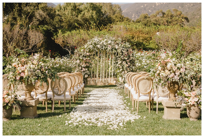 Garden ceremony at San Ysidro ranch with large floral arch and vintage chairs