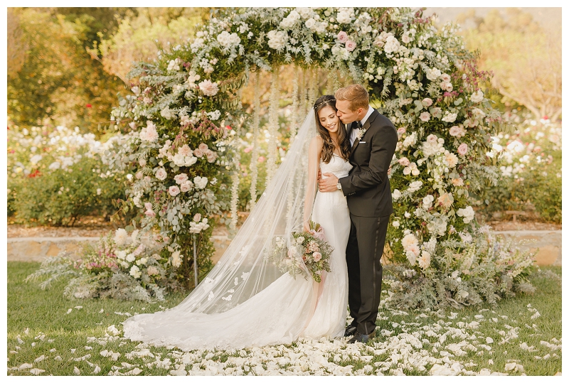 Bride and Groom standing under floral wedding arch at San Ysidro Ranch