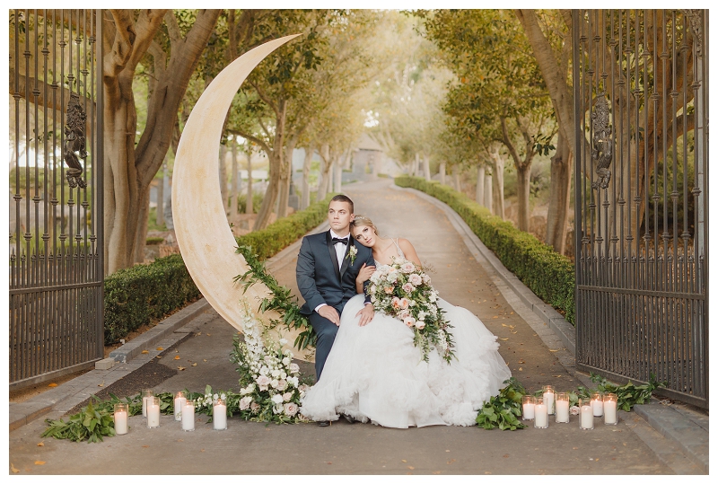 bride and groom sit on moon prop at their pastel styled Whimsical Enchanted Forest Wedding